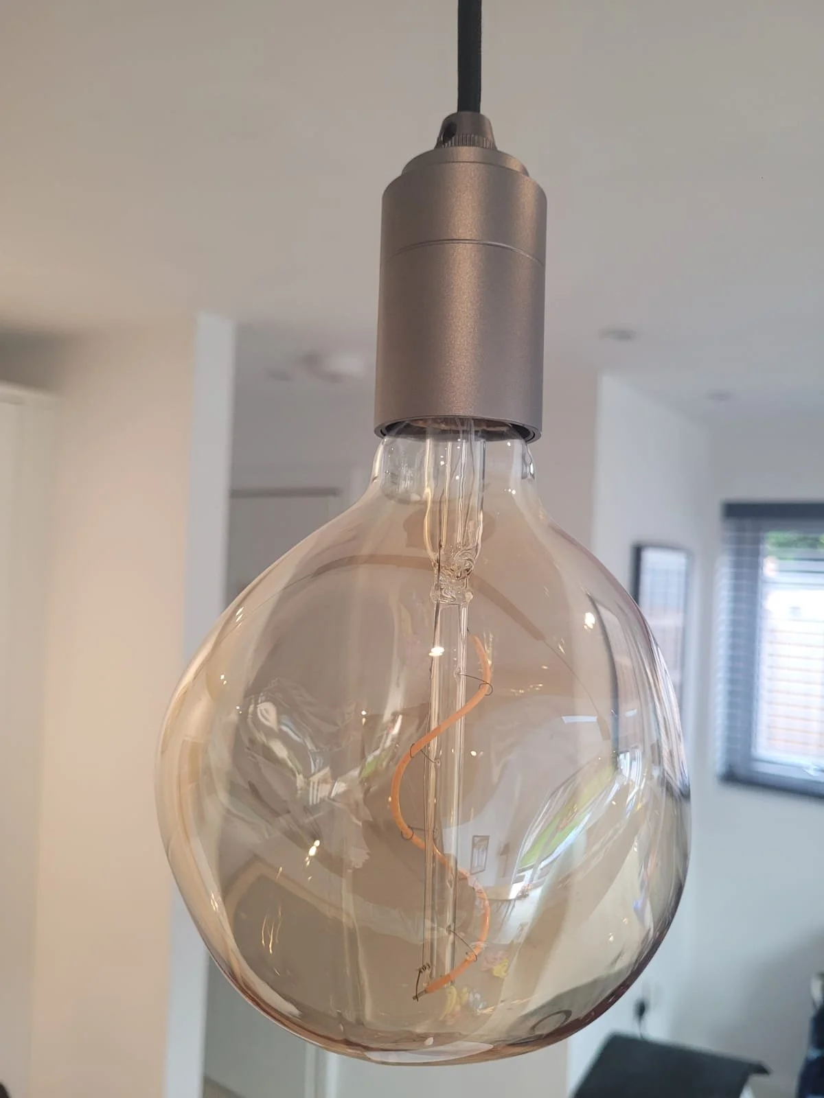 Close-up of a decorative ceiling light fixture with a clear, round glass bulb and a visible filament inside, hanging in a modern interior space.