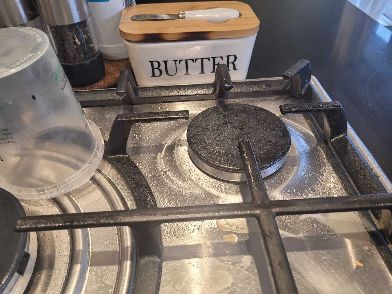 Empty stovetop with soapy residue, a container labeled 'BUTTER', and various kitchen items in the background.