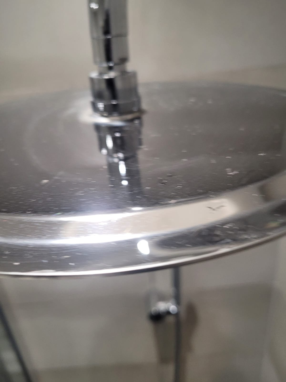 Close-up of a metallic water fountain spout with a water stream extending downward.