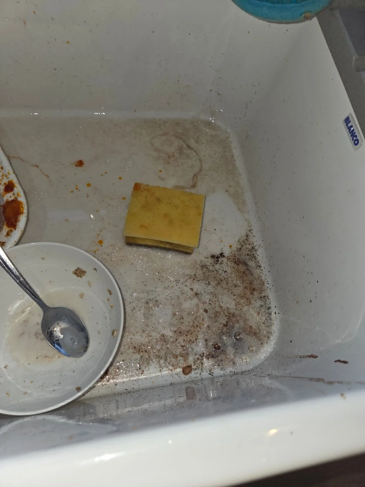 Empty and messy refrigerator with leftover crumbs, a sponge, and a small dish with a spoon inside.