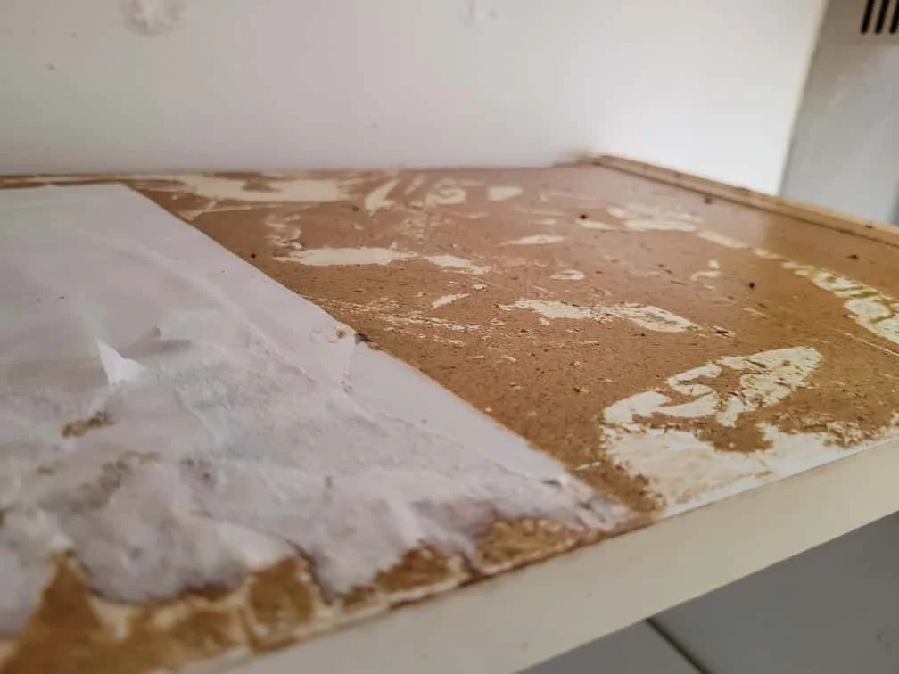 A wooden surface with peeling white paint and exposed brown wood, next to a white wall.