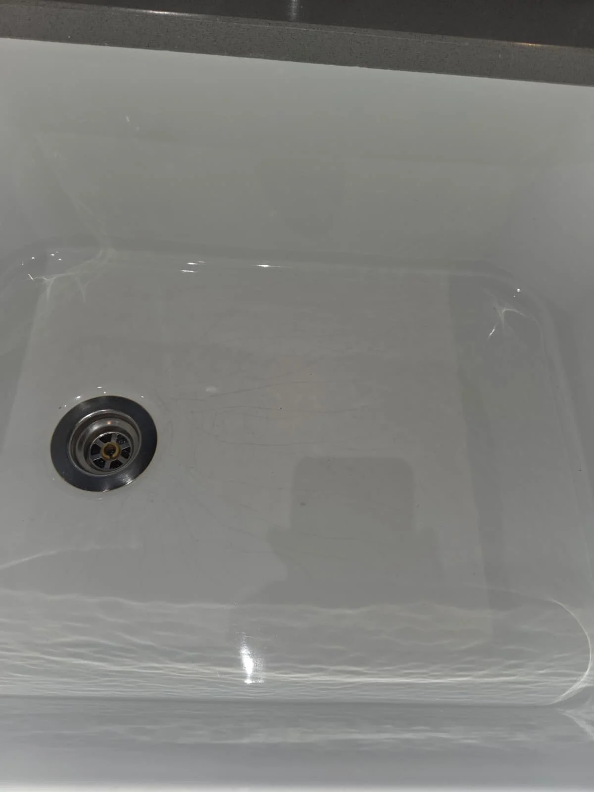 Empty white kitchen sink with a silver drain and a black rubber gasket.