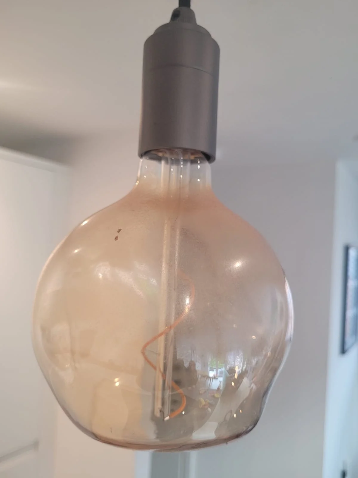 Close-up of a decorative Edison-style light bulb hanging from the ceiling in a room.