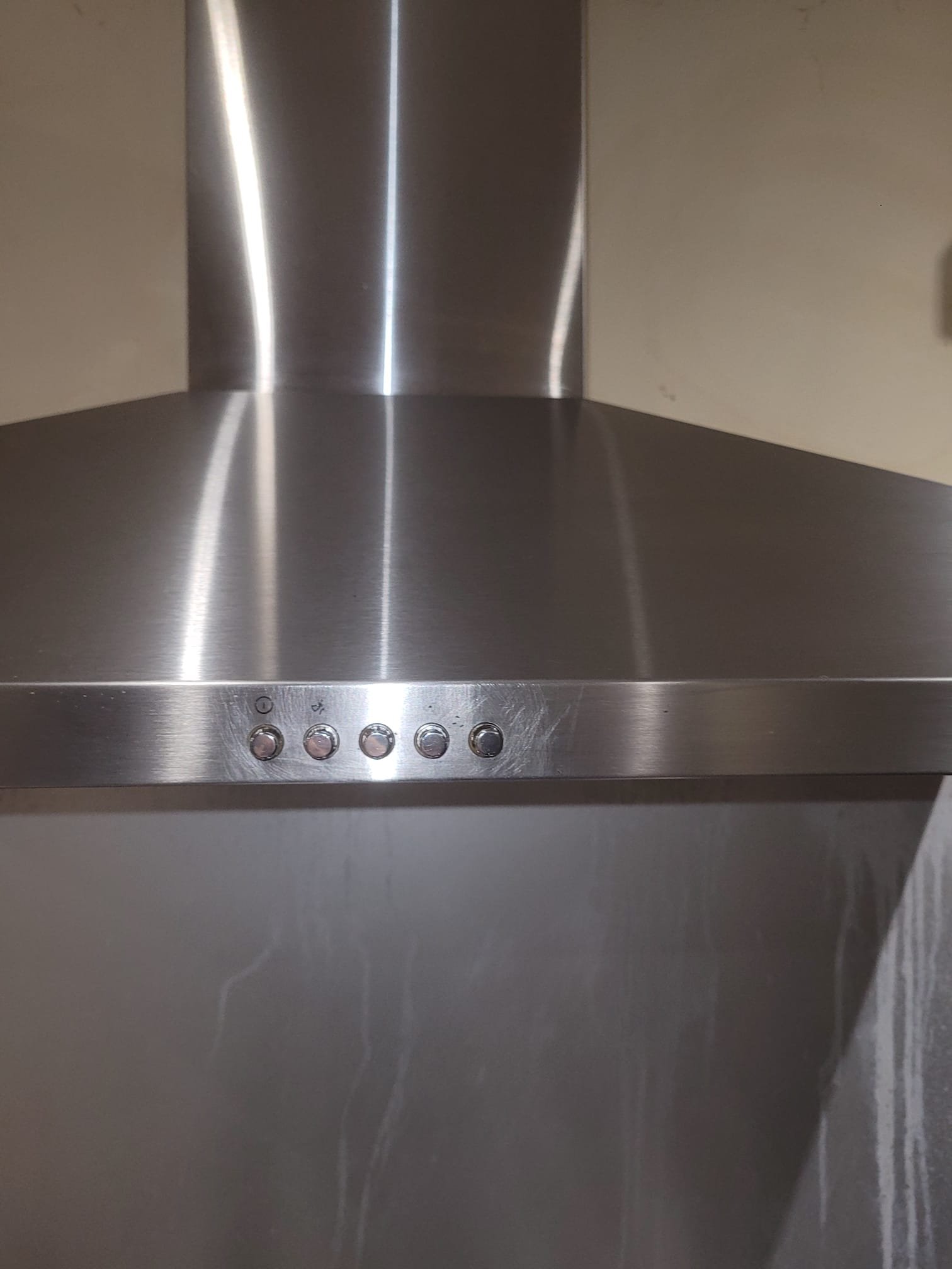 Close-up of a stainless steel kitchen range hood, showing control buttons on the front edge.