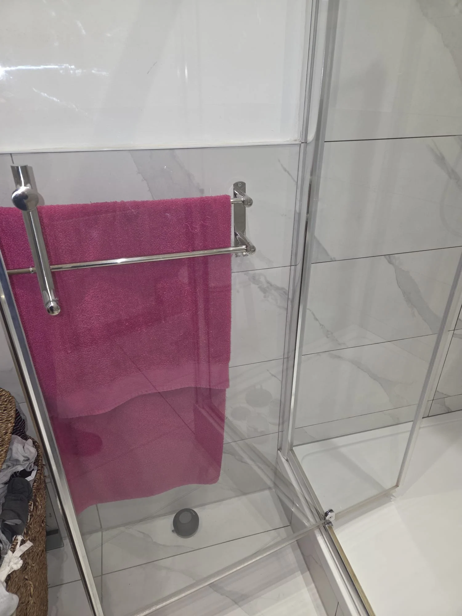 A bathroom shower enclosure with a pink towel hanging on a towel bar attached to the glass.