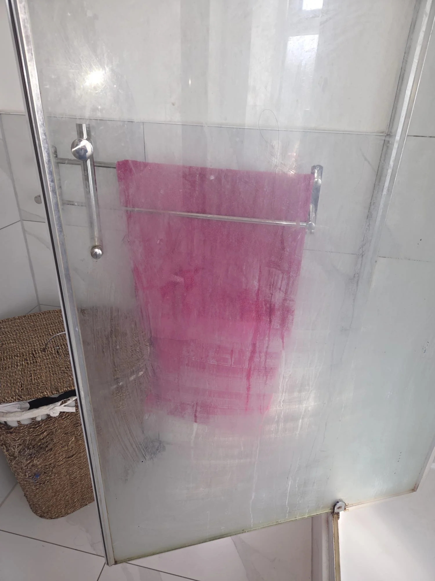 Frosted glass shower door with a pink towel hanging on a towel bar inside the shower.