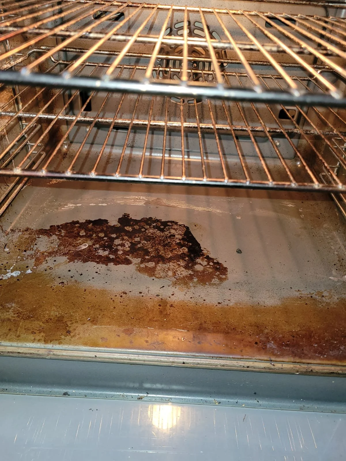 Inner part of a dirty oven with burnt food residue on the oven floor and oven racks.