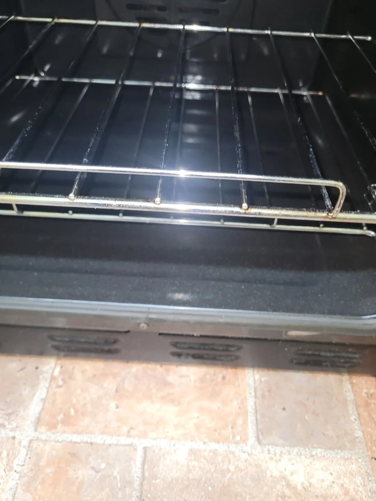 Inside view of a black oven with metal racks, with tiled floor visible at the bottom.