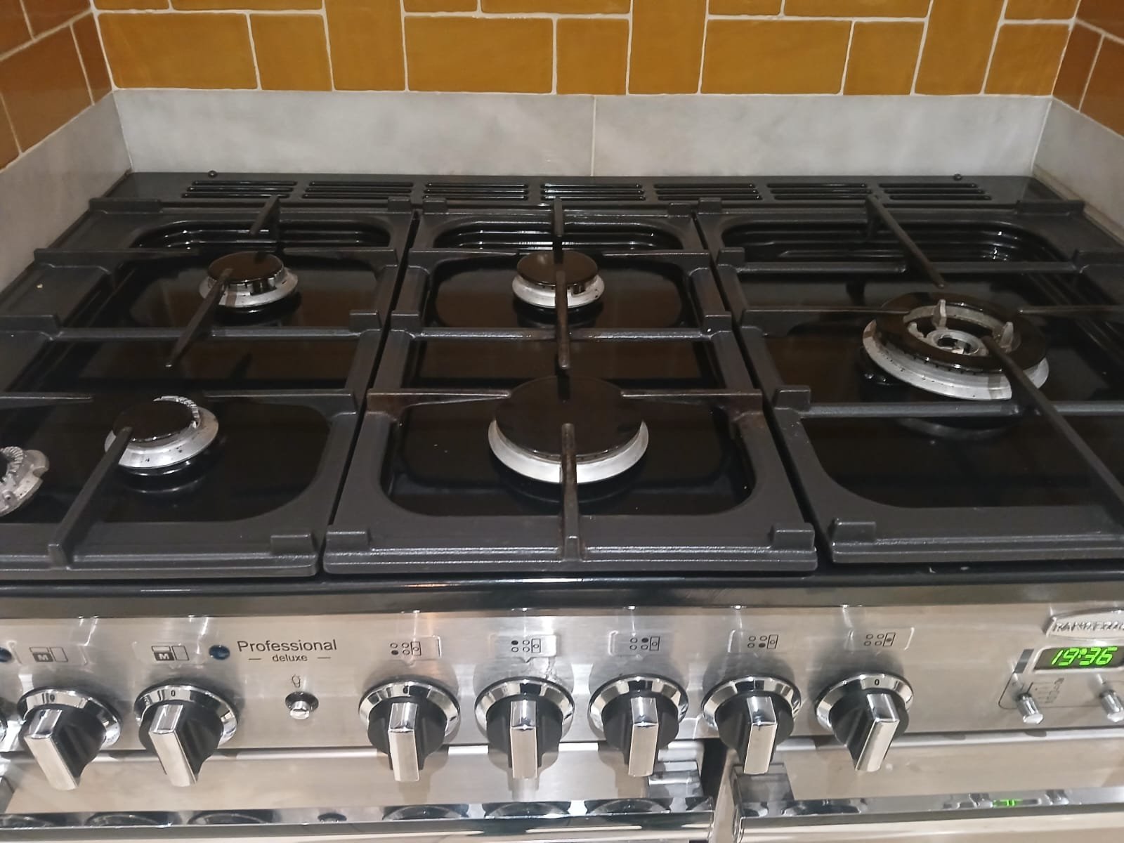 Stainless steel gas stove with five burners and metal control knobs, with a digital clock displaying 19:26.