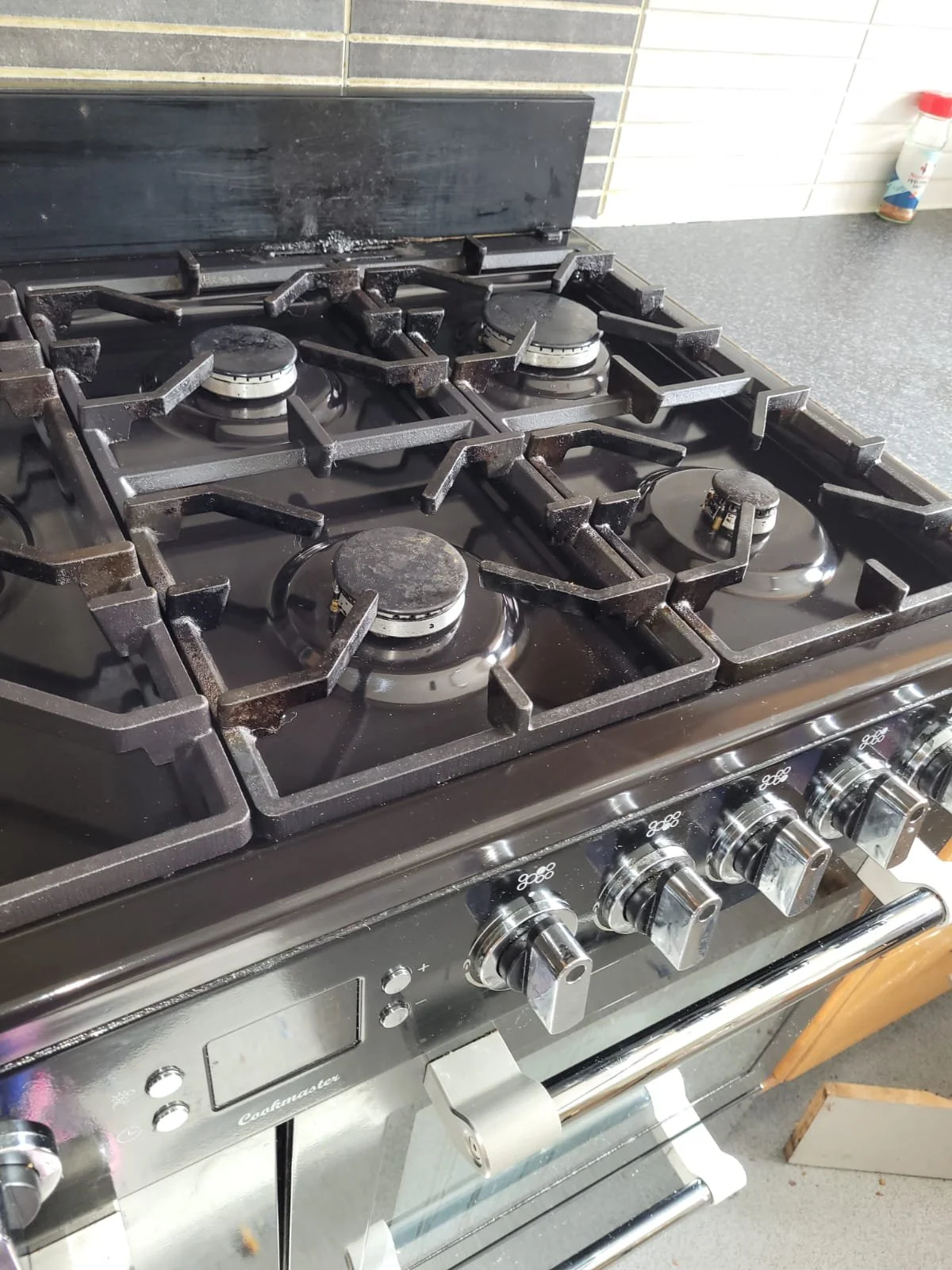 A black stainless steel gas stove with four burners, some of which have blackened, worn-out grates, and a control panel with four metal knobs.