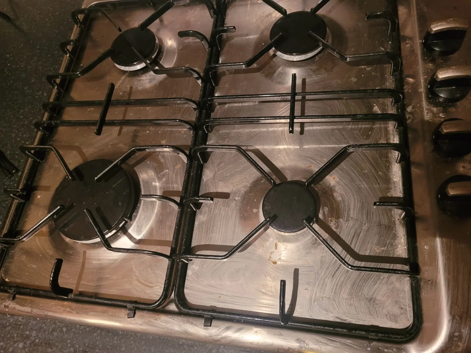 A stainless steel stove top with four gas burners, each with black metal grates and control knobs on the right side.