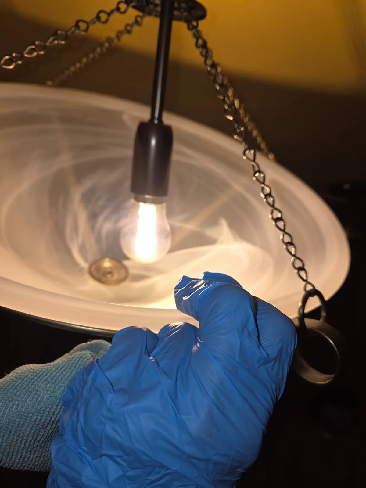 A person wearing a blue glove holding a chain with a key attached, hanging above a lit ceiling fixture.
