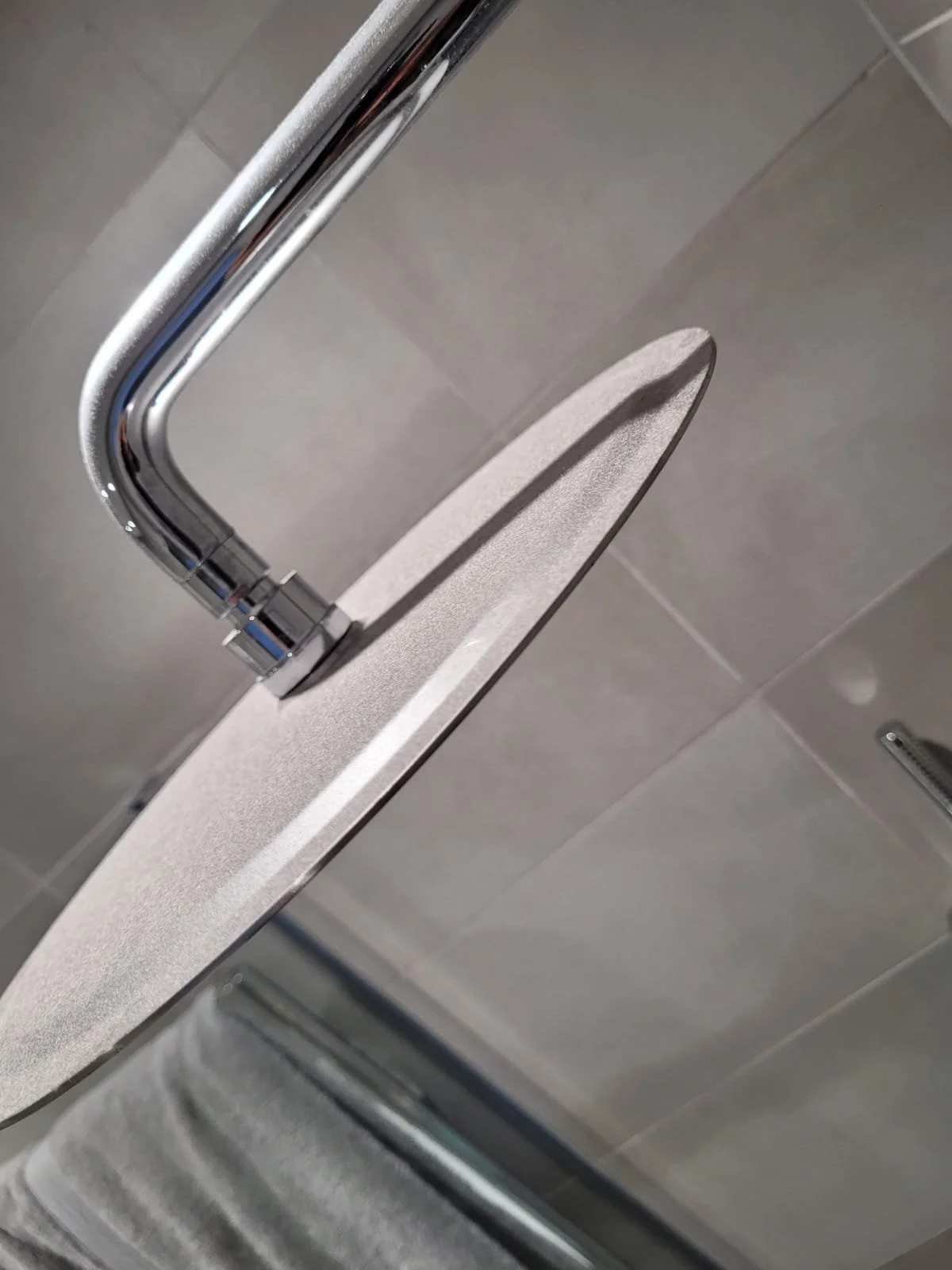 Close-up of a modern bathroom shower with a handheld shower head, a flat soap dish, and a glass shower door.