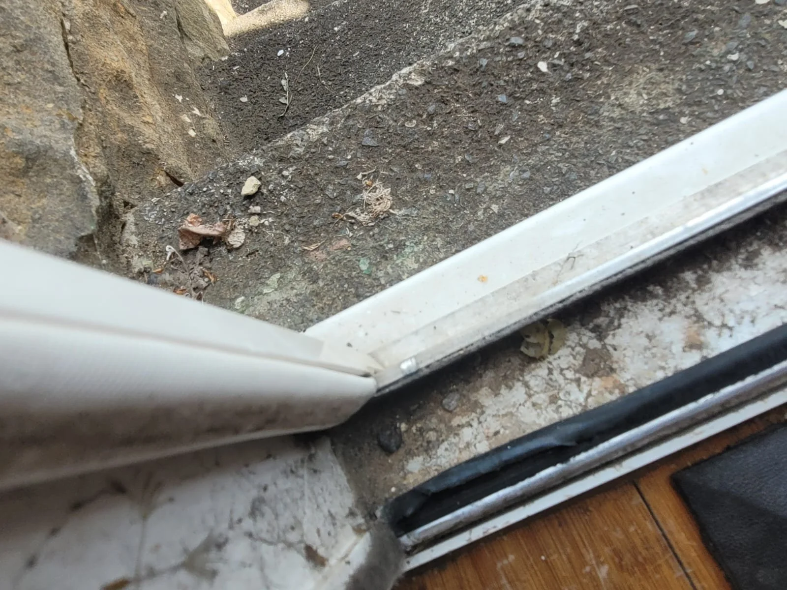 Close-up view of a dirty door threshold and window sill, with visible dirt, dust, and debris on the surface.