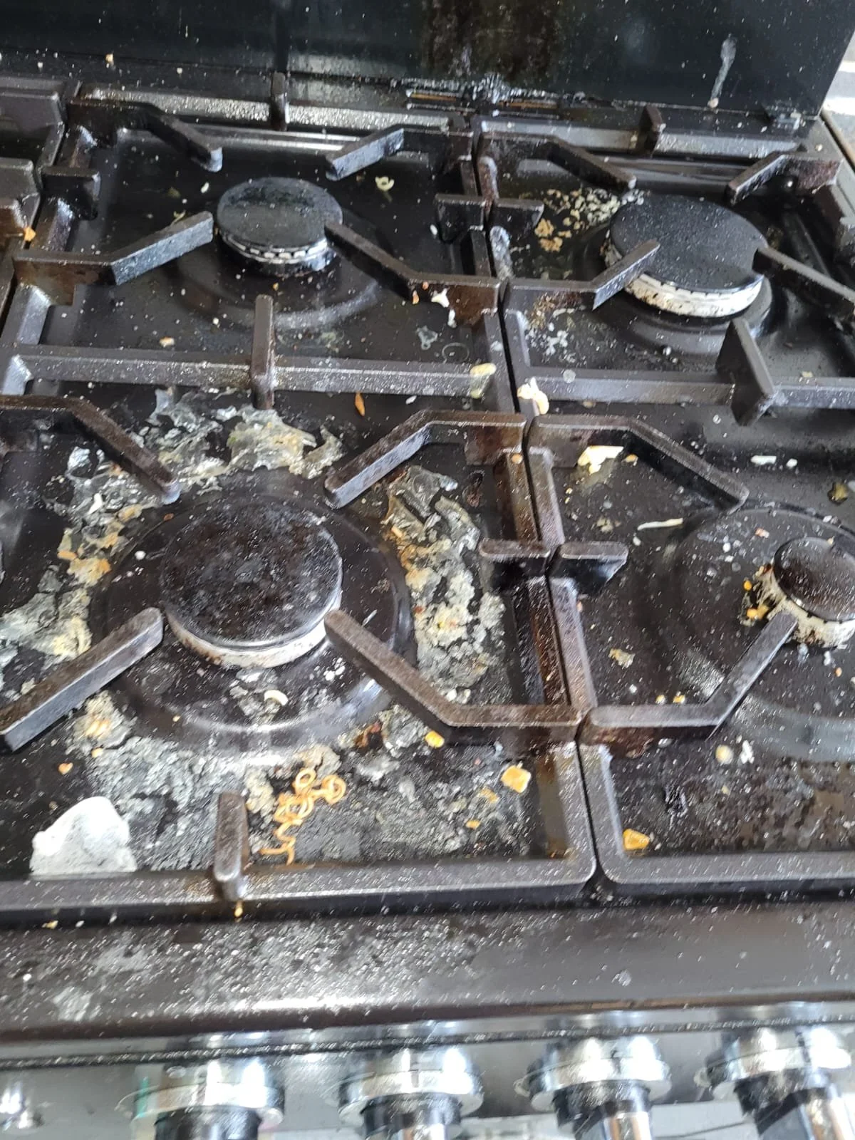 Dirty stovetop with burnt food, grease, and crumbs on burners and around the surface.