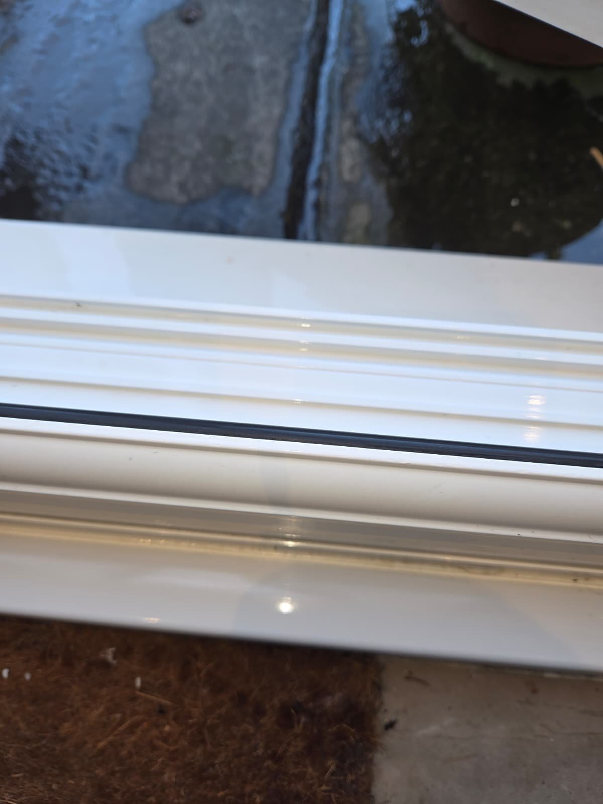 Close-up view of a window with a white frame, showing part of the glass and a brown and black object outside, possibly a rock or part of a structure.
