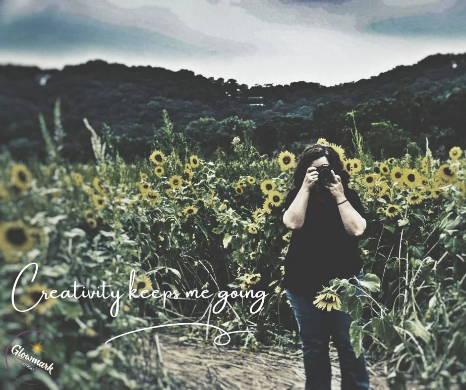 Person taking a photo in a sunflower field with mountains in the background and a quote that says, 'Creativity keeps me going.'