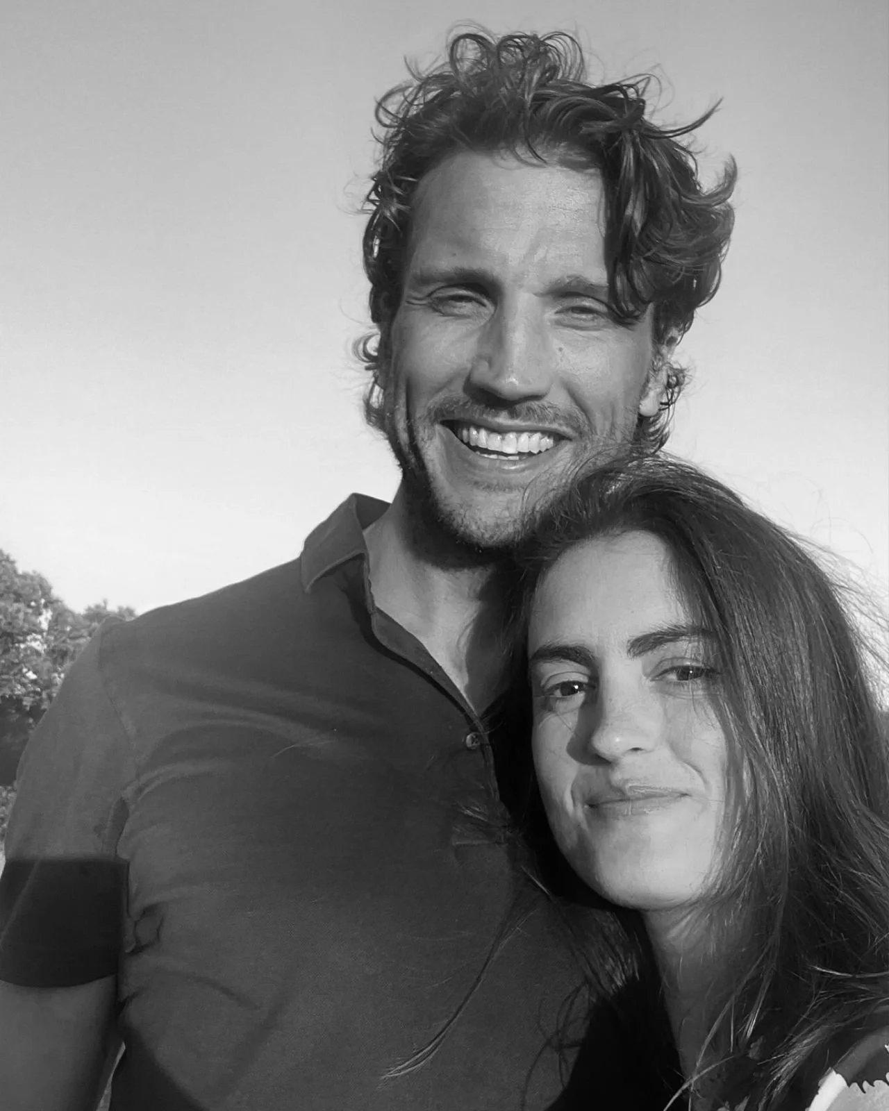 Una coppia sorridente, un uomo con capelli ricci e barba e una donna con capelli lunghi e mossi, abbracciati all'aperto.