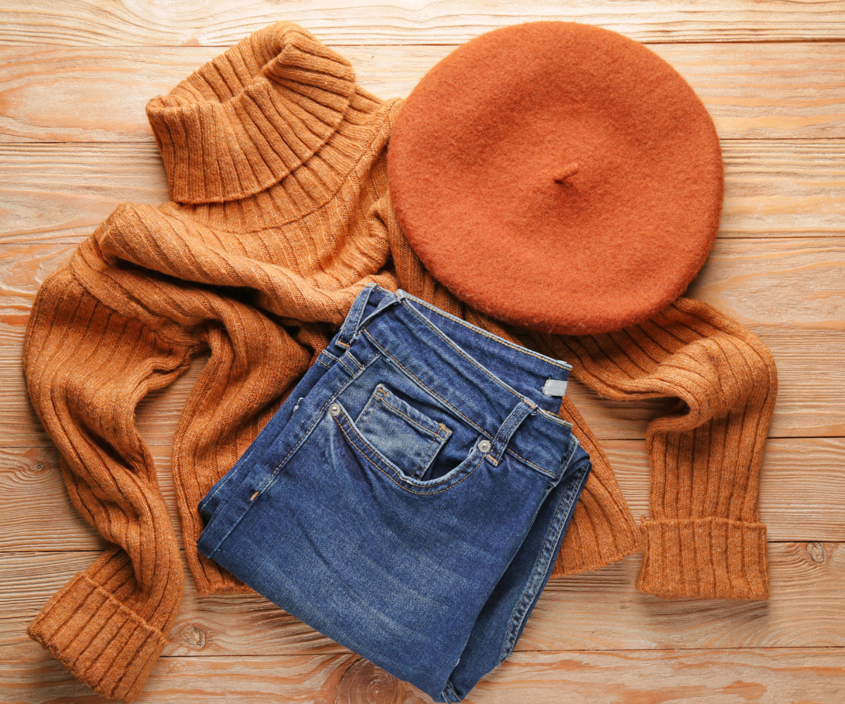 Rõivakomplekt, mis koosneb pruunist soonikuga kõrge kaelusega kampsunist, samas toonis barettist ja sinistest teksapükstest, asetatud puidust pinnale.