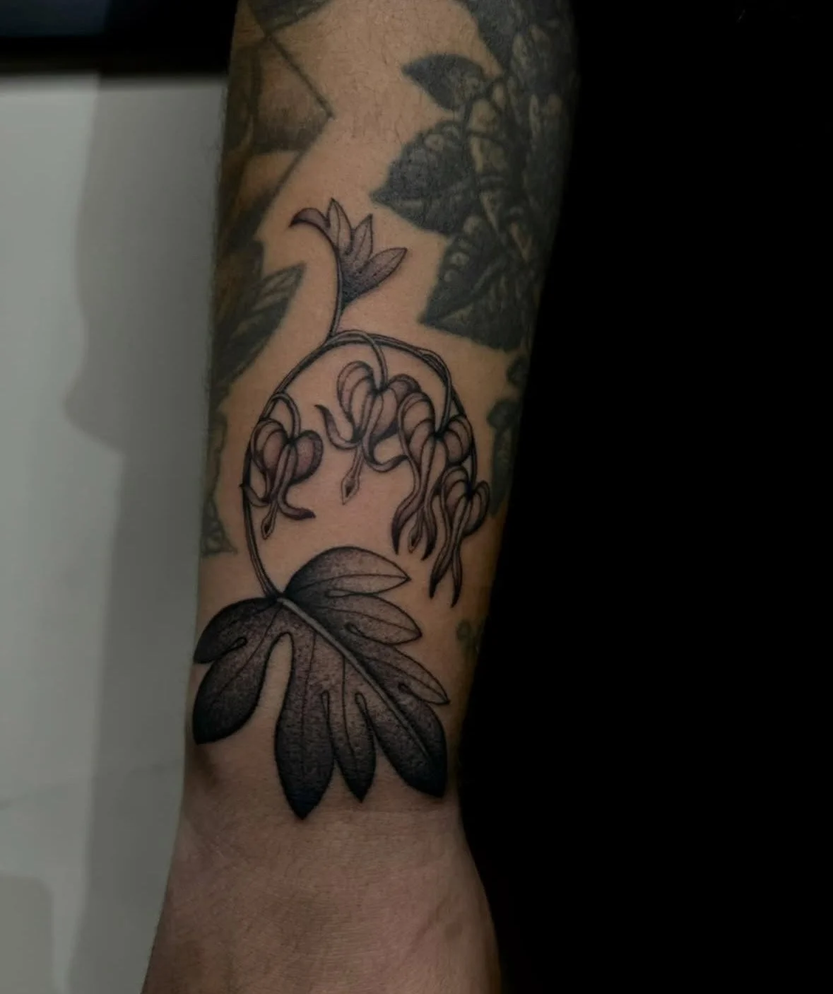 Tattoo of a large leaf and hanging flowers on a person's forearm.