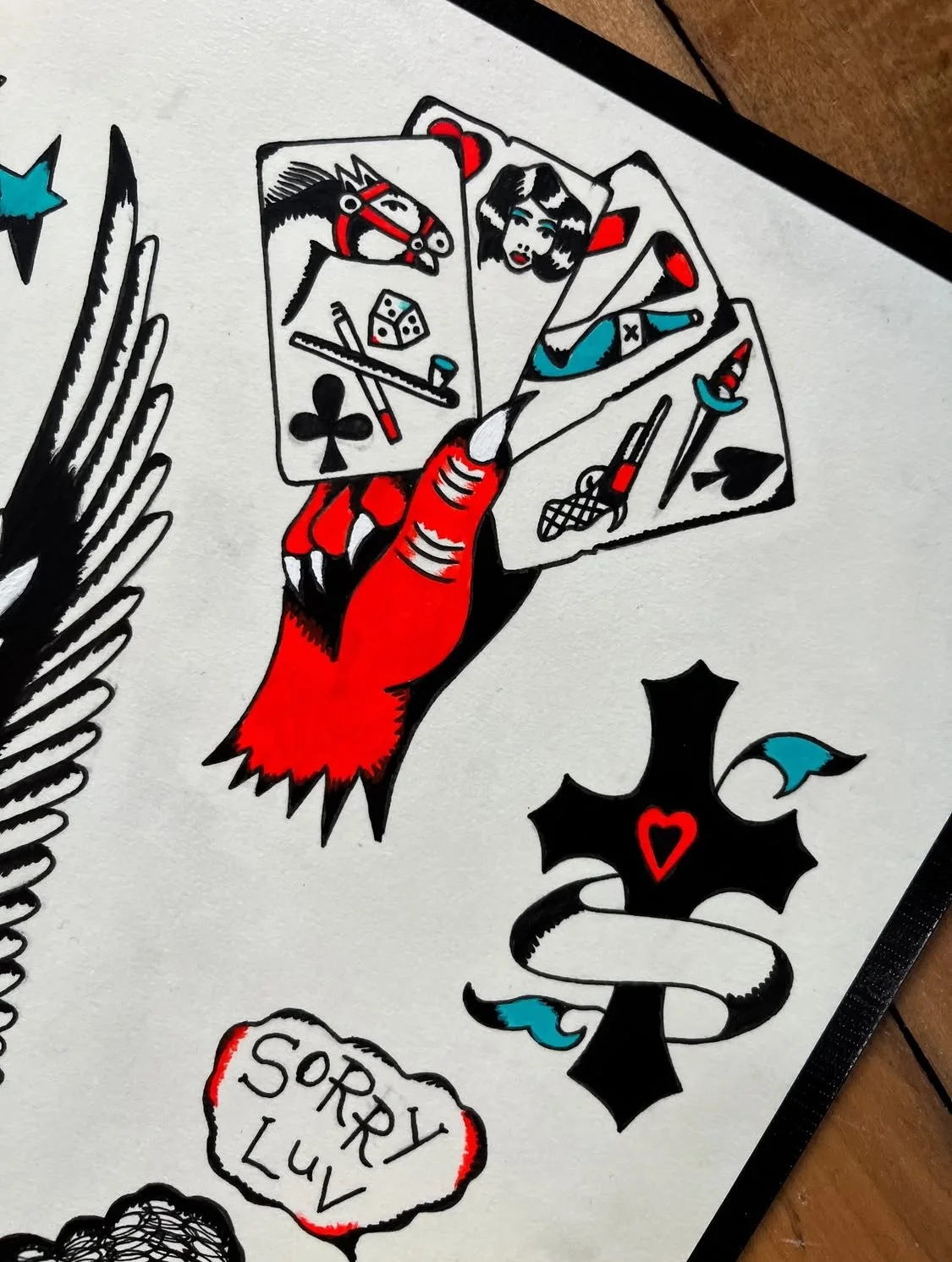 Tattoo-style drawing of a hand holding four playing cards, with a black spade symbol and a red heart symbol below, along with a speech bubble reading 'SORRY LV'.