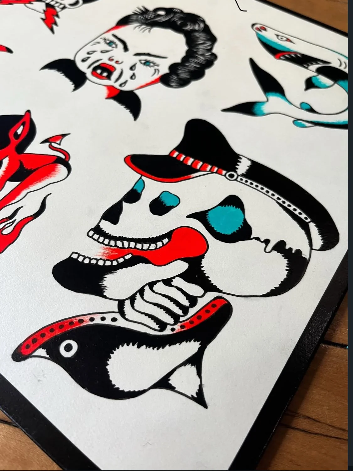 Tattoo flash sheet featuring various traditional tattoo designs, including a woman's face with tears, a shark, a skull with a cowboy hat, and a rabbit with a red bandana, in black, red, and blue colors.