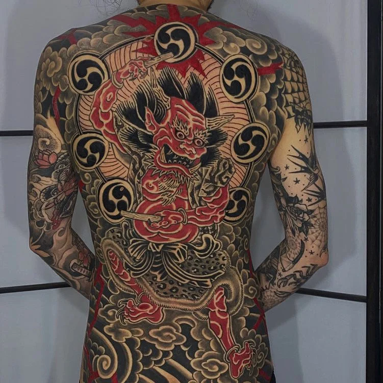 Full back of a person with extensive traditional Japanese-style tattoo featuring a fierce tiger, a dragon, and swirling clouds in black, red, and gold ink.