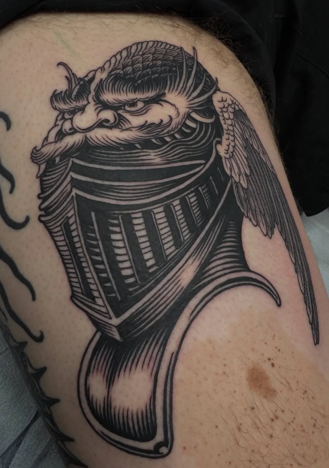 Black and gray tattoo of a fierce dragon's head with detailed scales, horns, and a long flowing mane on a person's upper arm.
