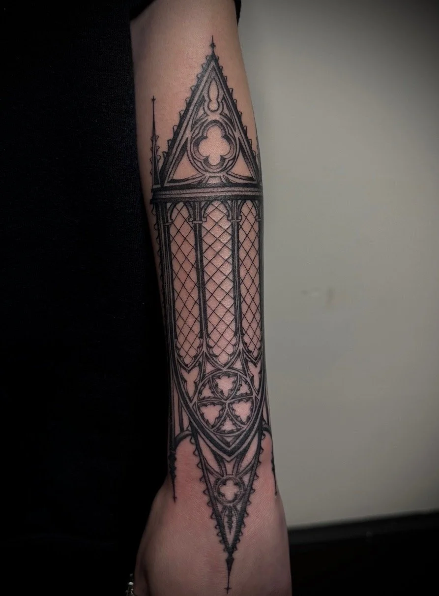 Black and gray tattoo of a Gothic cathedral window on a person's forearm.
