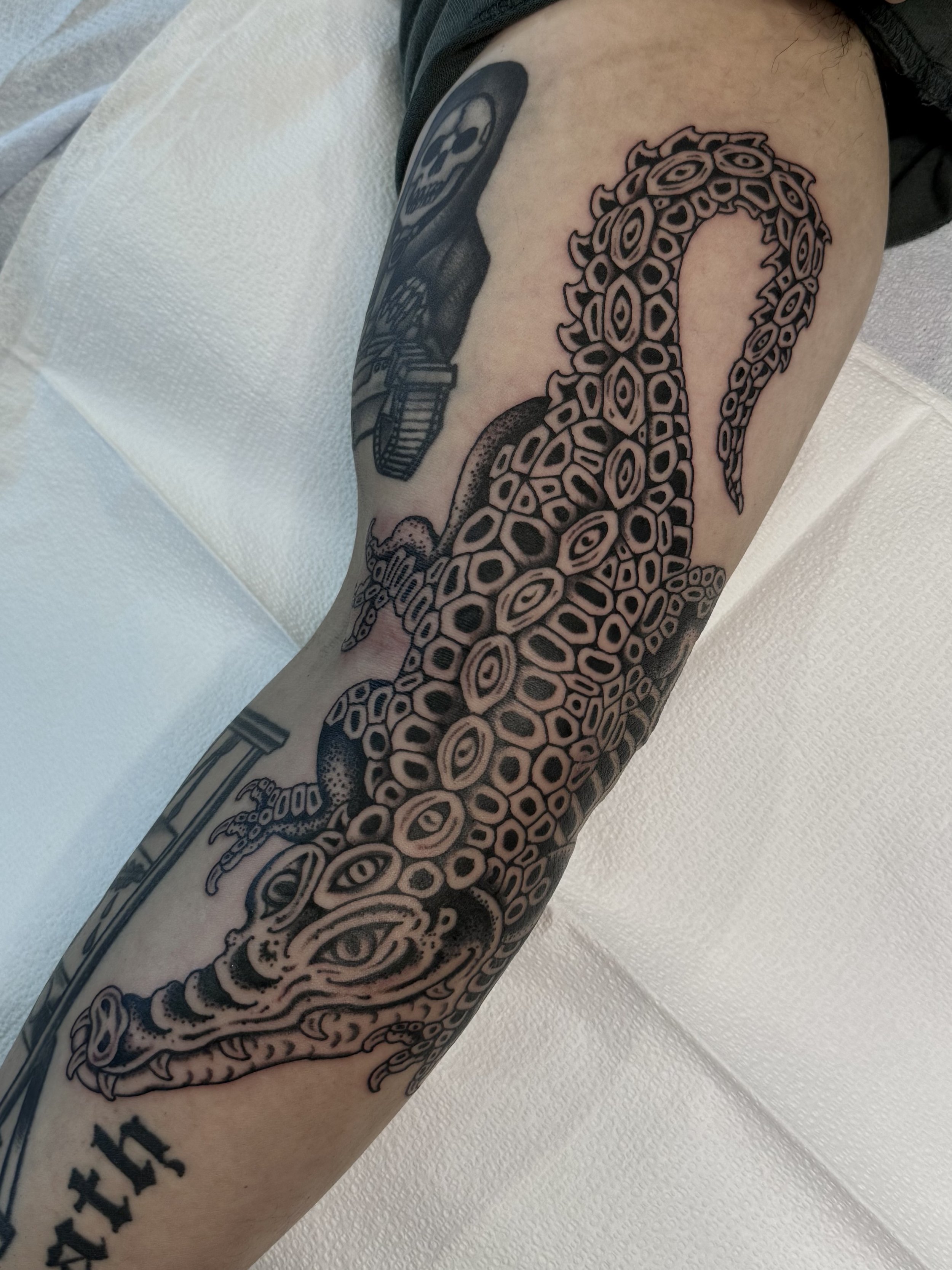 Tattoo of an octopus with multiple eyes on a person's arm, with a skull and other designs nearby.