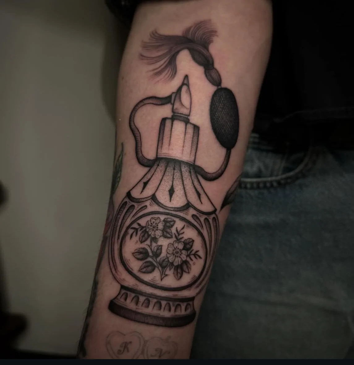 Tattoo of a vintage perfume bottle with a flower inside, connected to a microphone by a tube, with a woman's face in profile and flowing hair above.