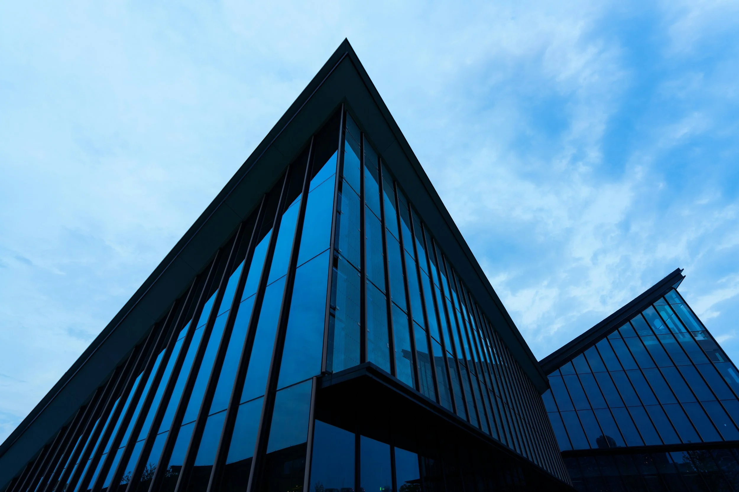 Modern glass skyscraper with reflective windows, set against a bright blue sky with wispy clouds.