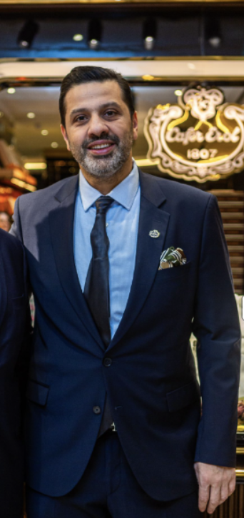 Man in a dark suit, light blue shirt, and dark tie standing in front of a restaurant sign.