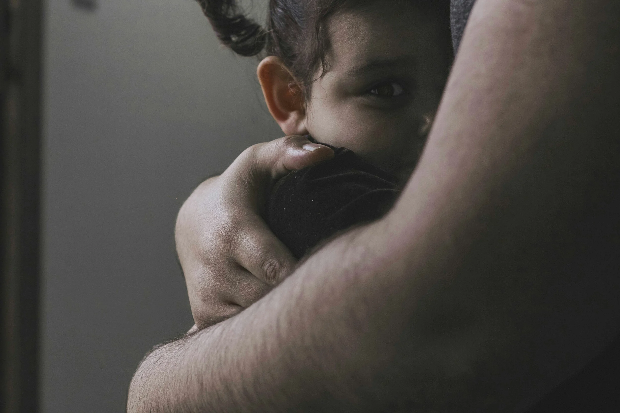 A person with dark hair embracing a young child, partially hidden, inside a close-up shot.