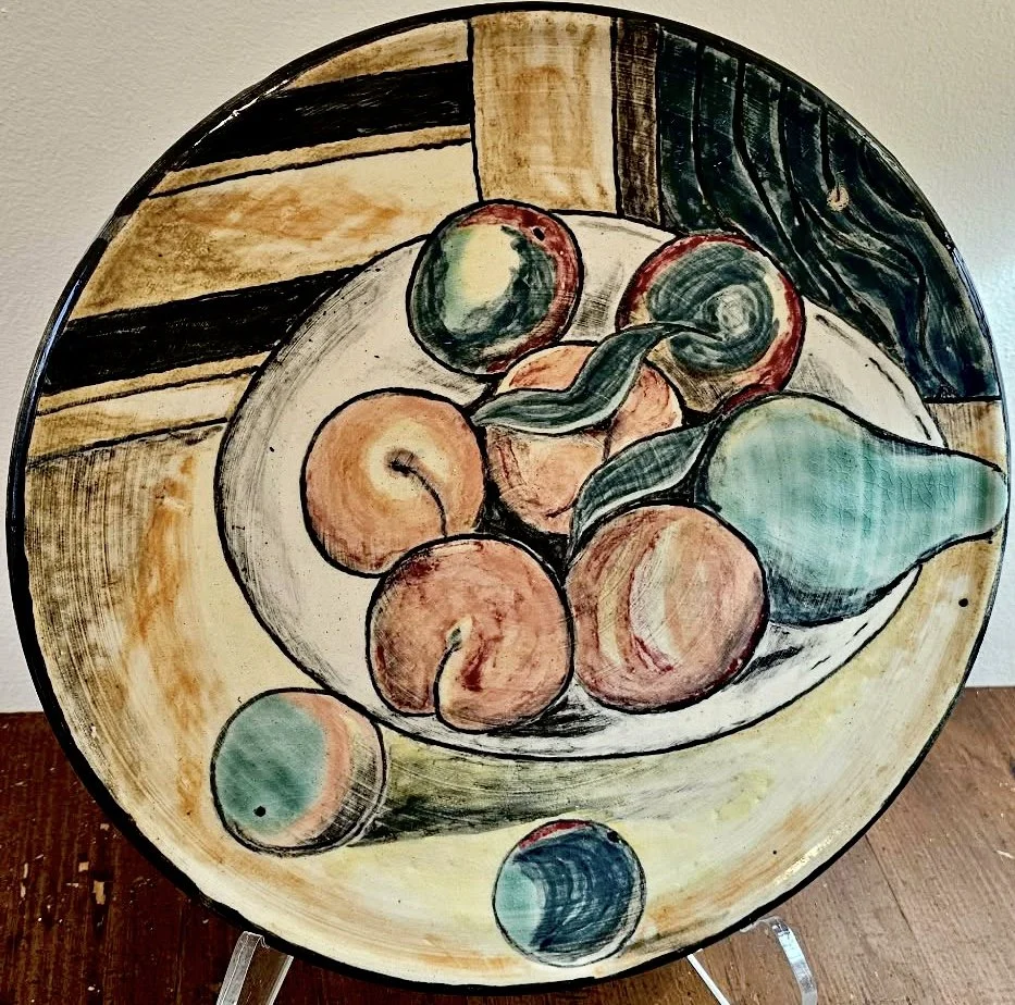 A decorative ceramic plate with a fruit still life painting, including peaches, pears, and other round fruits, with a background featuring hand-painted geometric patterns.
