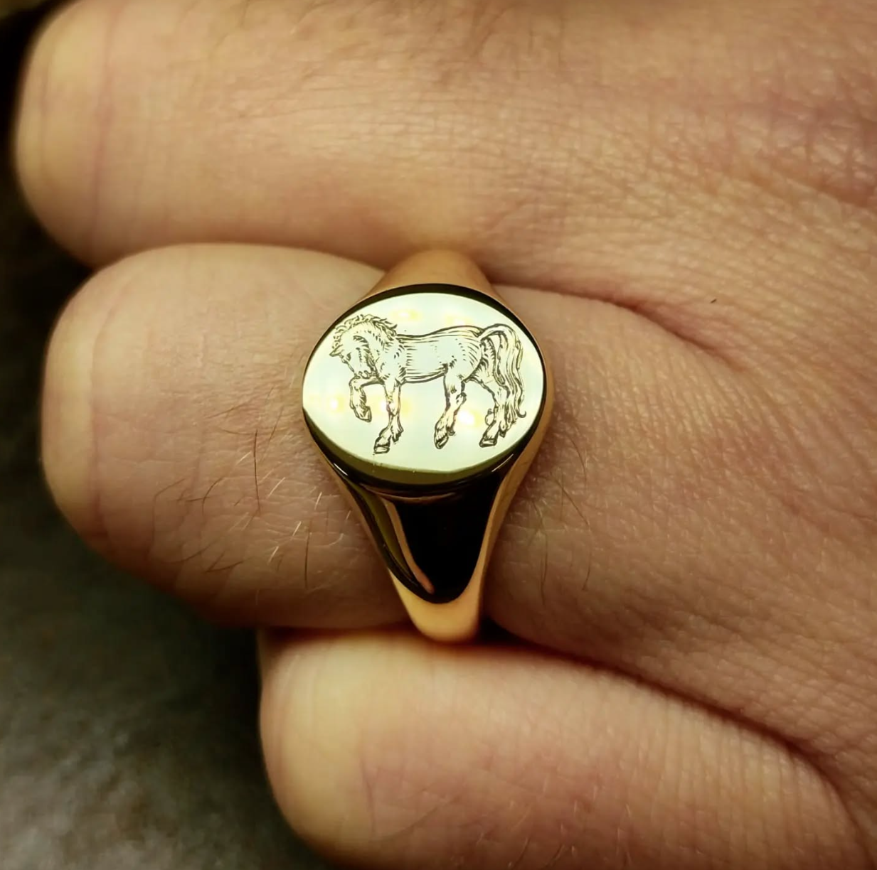 A gold ring with a circular face featuring an engraved outline of a horse.
