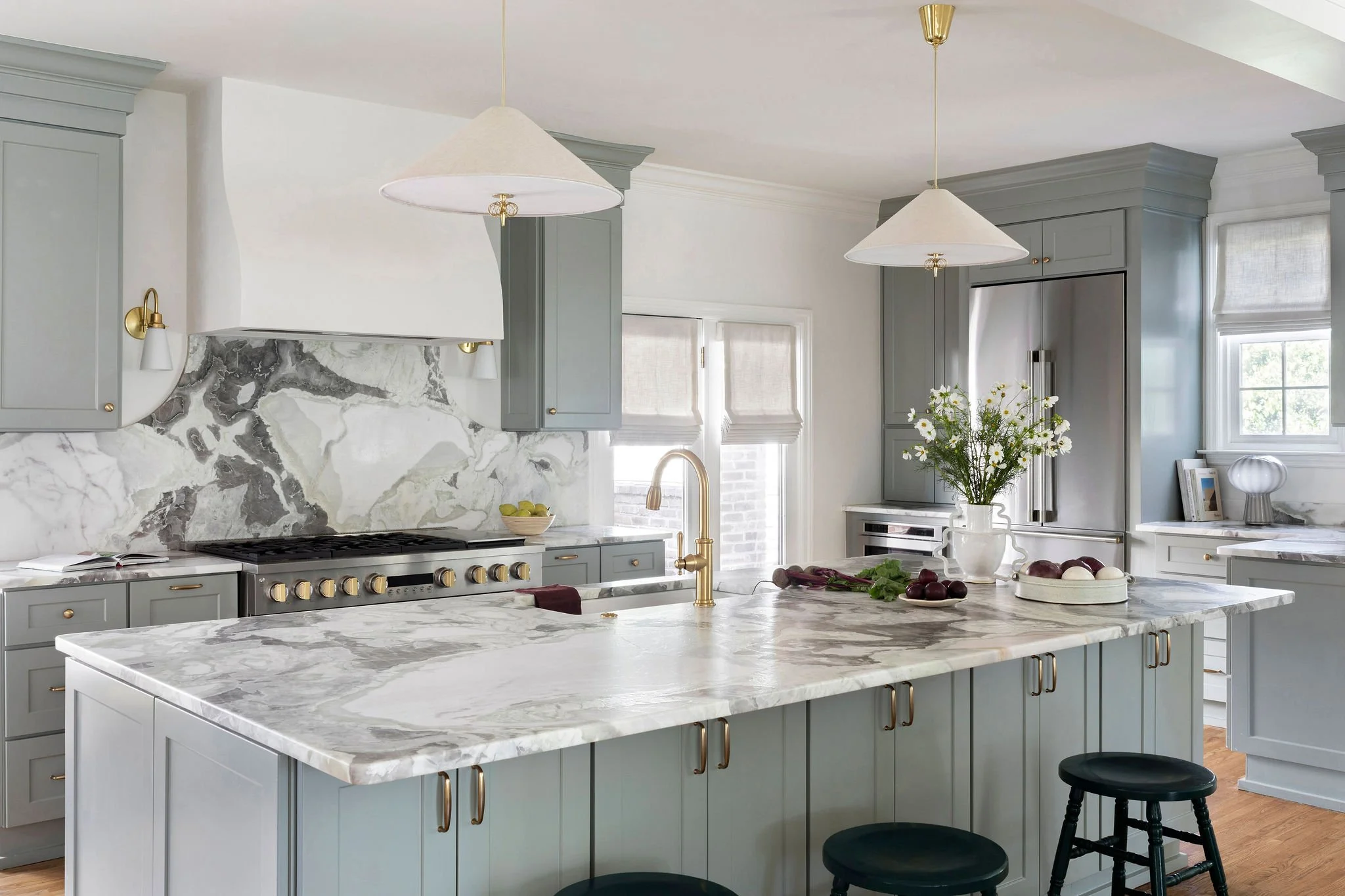 Modern transitional kitchen in Nashville featuring light green cabinetry, a large marble island, and brass hardware