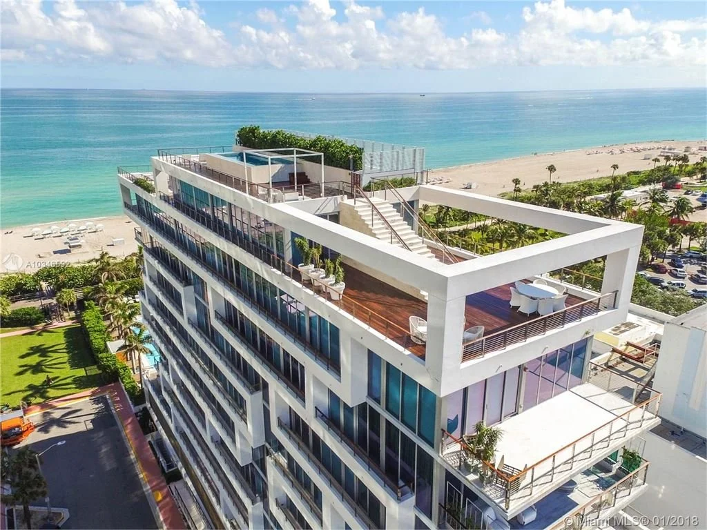 Aerial view of a modern beachfront hotel with multiple balconies and rooftop terrace overlooking the ocean.