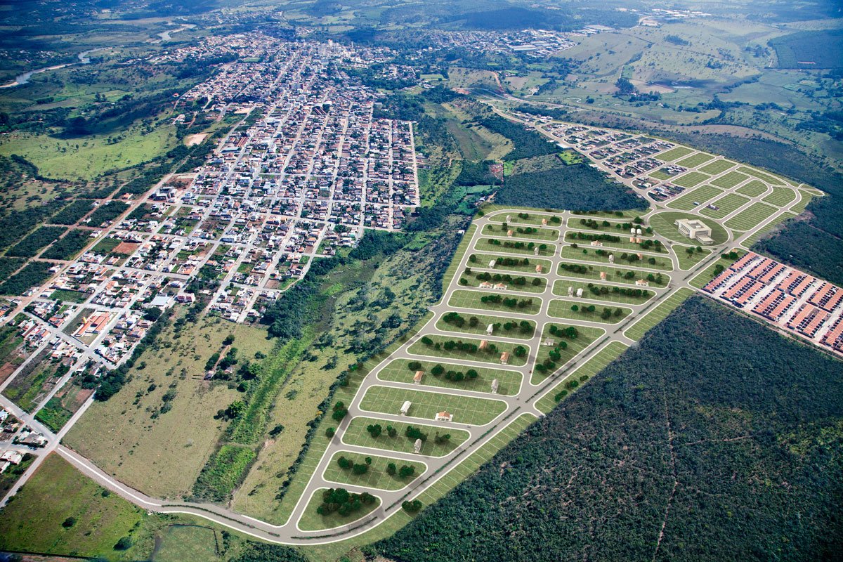 Aerial view of a small town and a new development with roads and lots for homes, surrounded by green hills and forests.