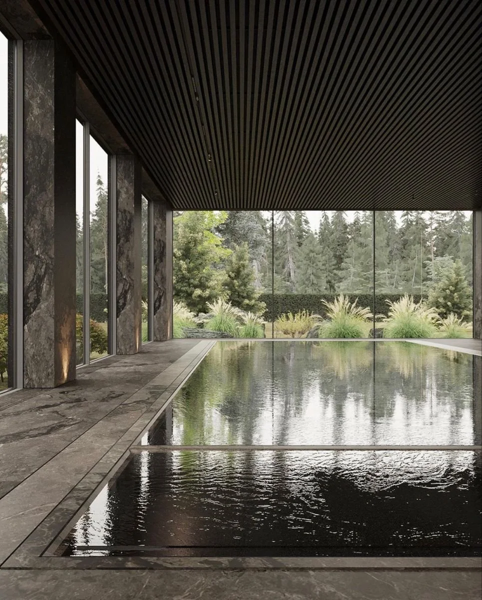 Indoor pool area with large floor-to-ceiling windows revealing a garden outside, dark ceiling with wooden slats, marble walls, and a calm reflective water surface.