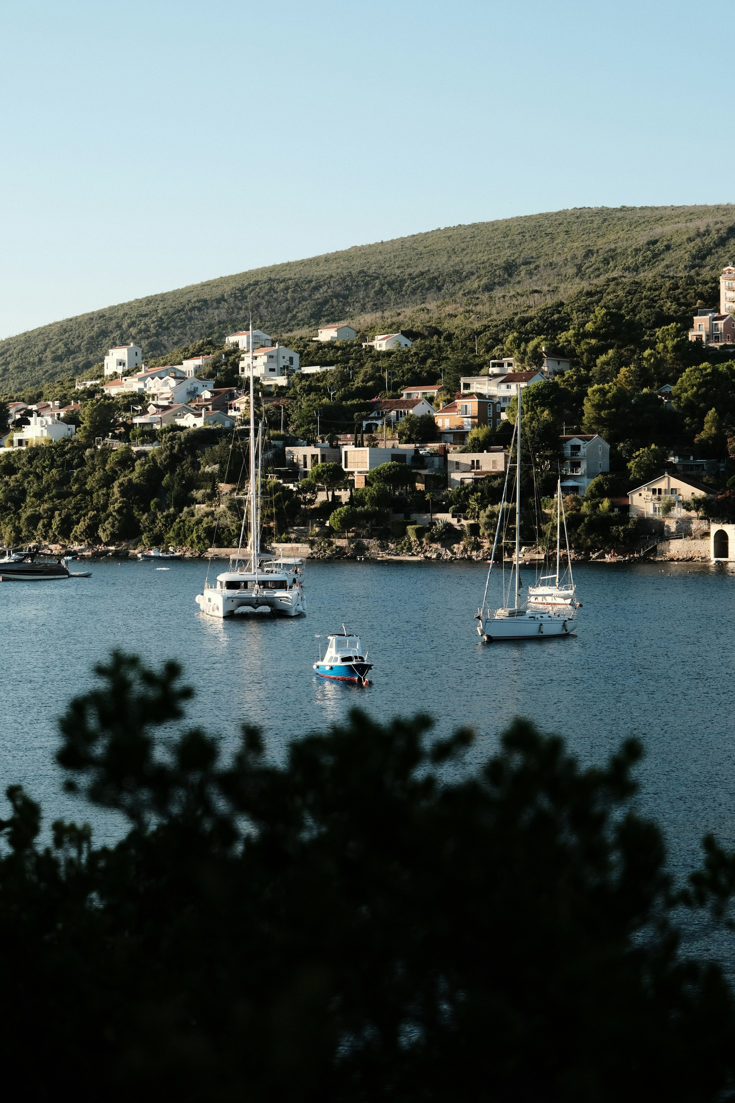 Boats anchored in a peaceful bay with hills and houses in the background.