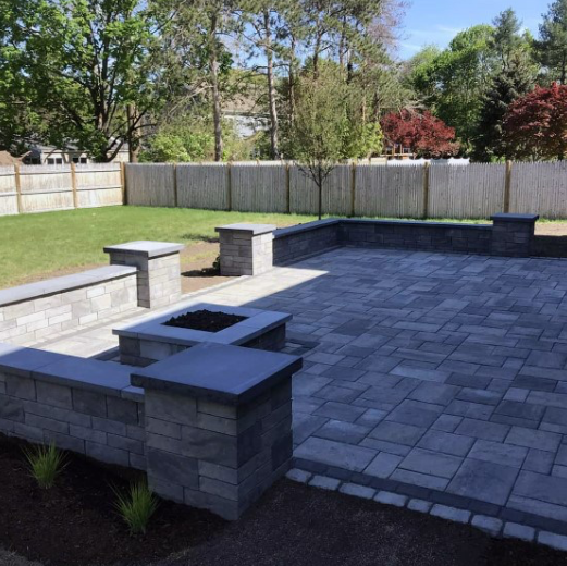 Spacious backyard with a newly paved stone patio, low stone walls with built-in planters.