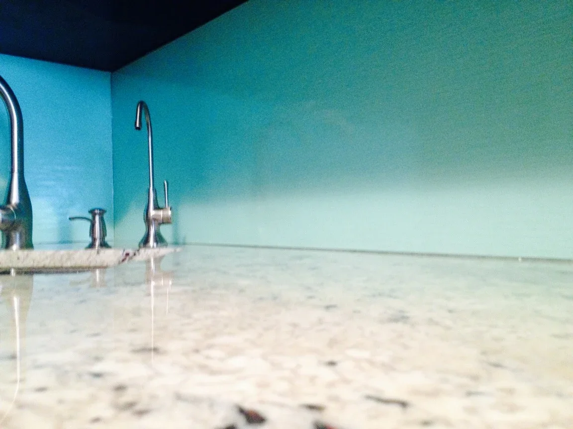 Close-up view of a kitchen countertop with three stainless steel faucets and a blue wall behind them.