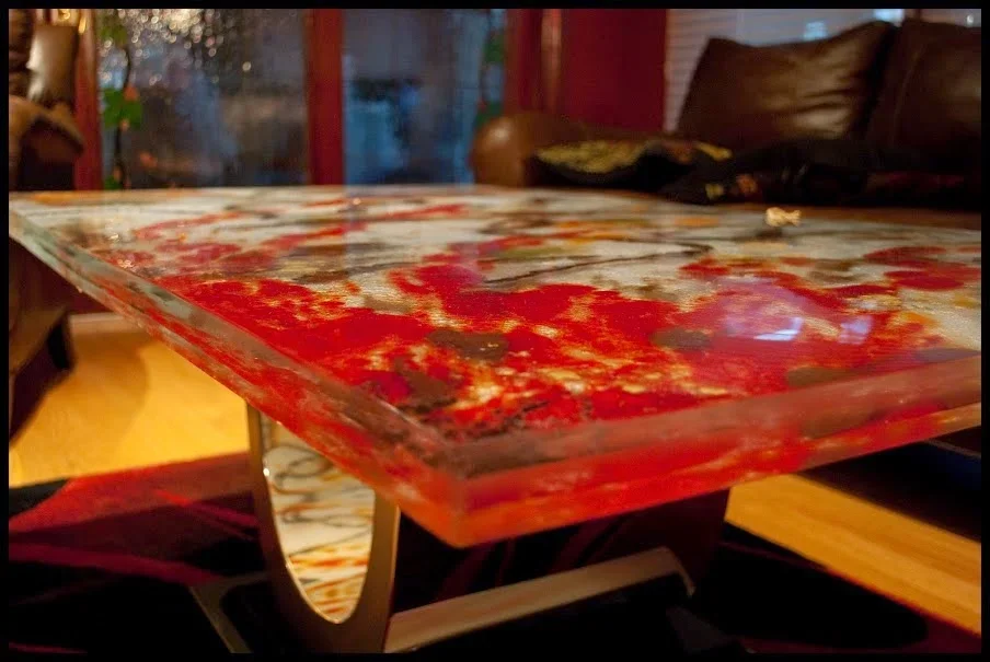 Close-up of a colorful, abstract-patterned glass table with a blurred living room background.
