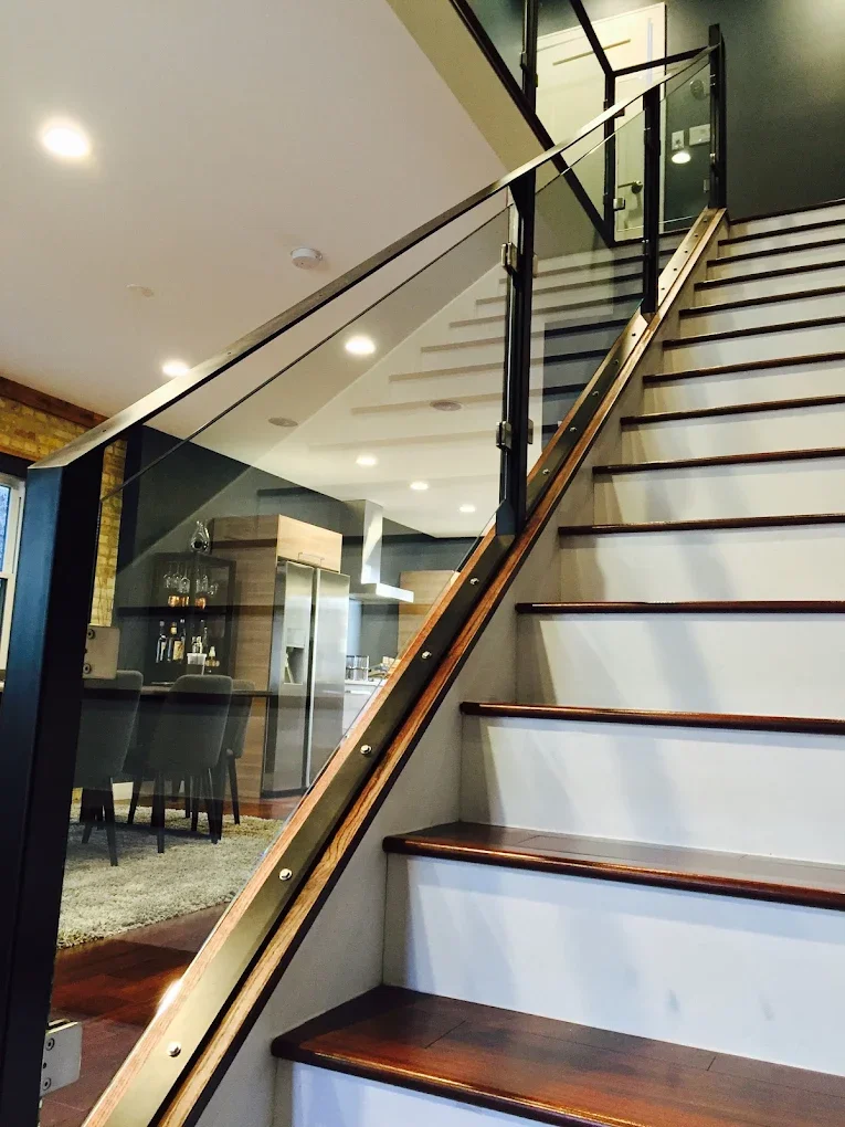 Indoor staircase with wooden steps, glass railing, and black metal supports in a modern home interior.