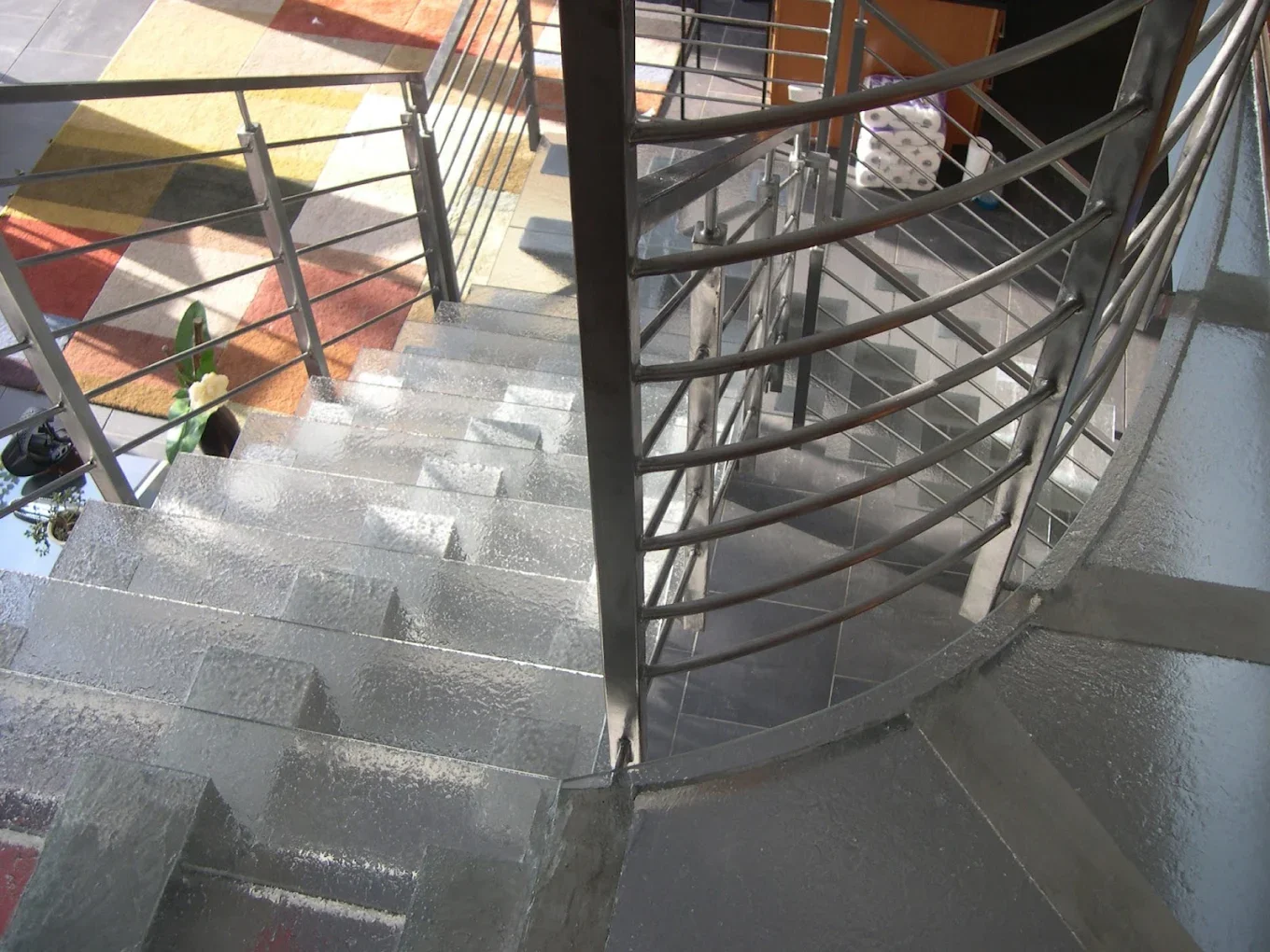 Indoor metal staircase with curved railings and a colorful geometric rug at the bottom.