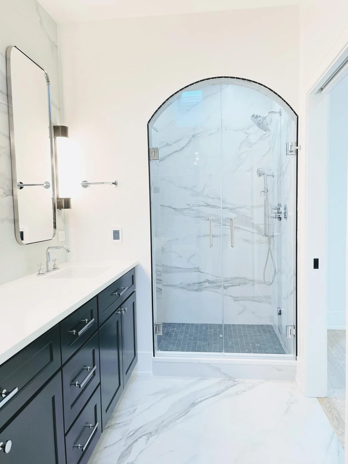 Modern bathroom with a glass shower enclosure, marble walls and flooring, a vanity with a mirror and cabinetry.