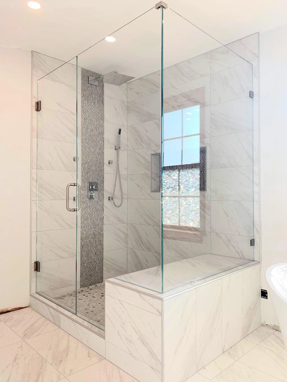 A modern glass-enclosed shower with marble tiles, a rainfall showerhead, and a window with a colorful mosaic pattern in the background.