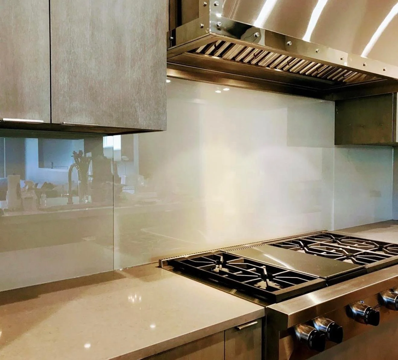 Close-up of a modern kitchen stove with four burners and a stainless steel range hood above. There are wooden cabinets and a reflective backsplash.