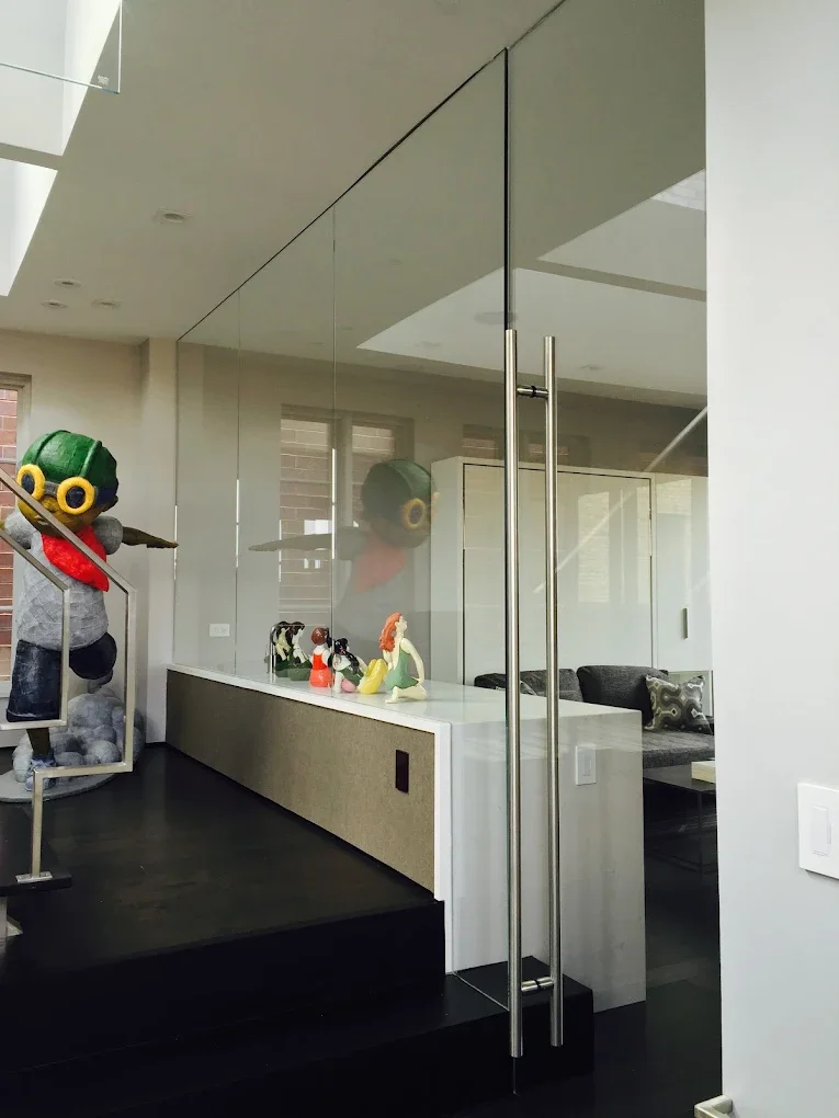 Interior view of a modern house with glass door, display of decorative figurines, and a seated area with a cushion.